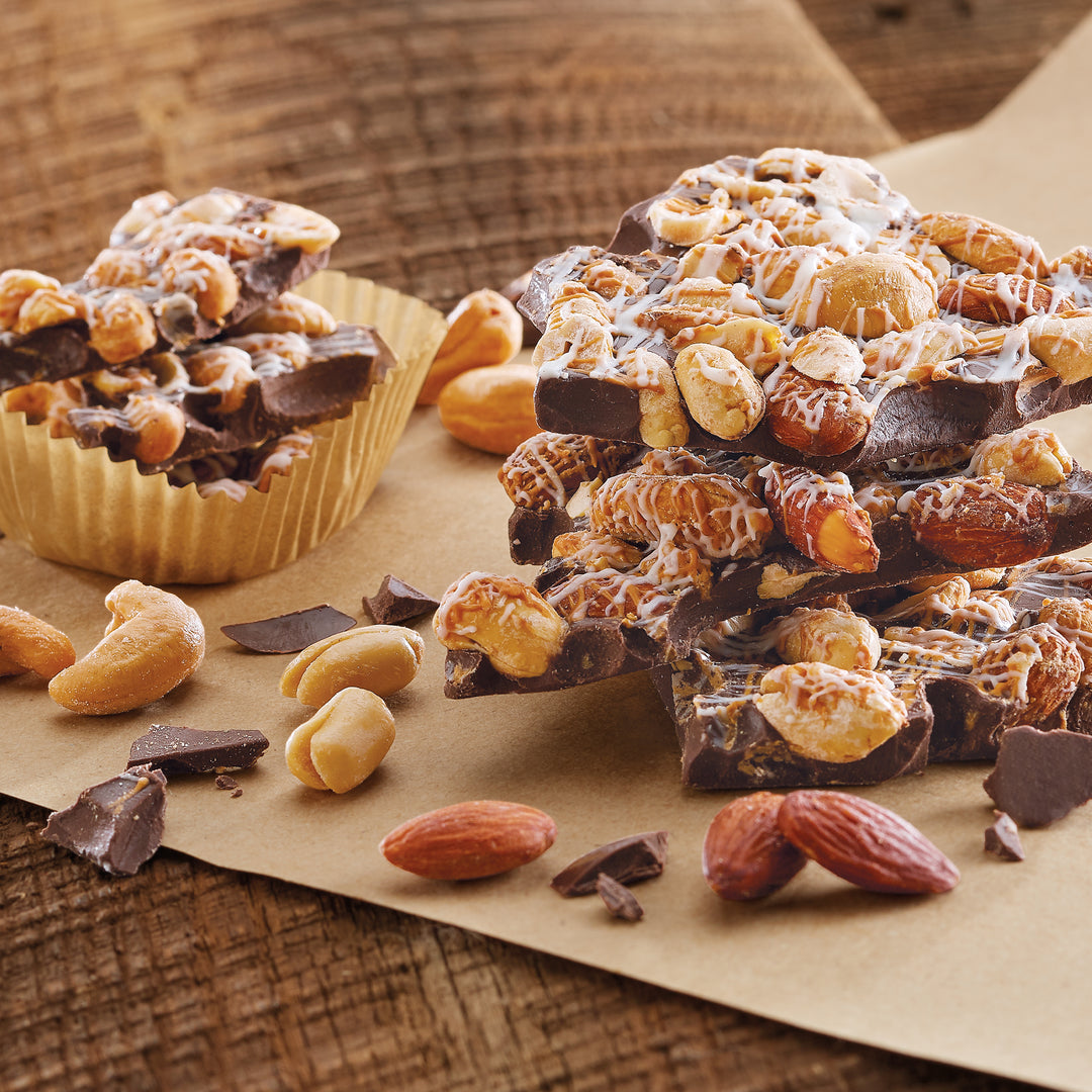 Whitley's Dark Chocolatey Bark Bites stacked and in paper cup with loose pieces surrounding on craft paper and linen tablecloth