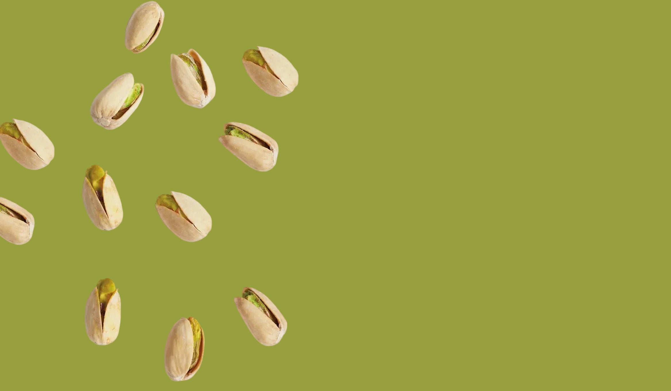 Whitley's pistachios scattered on a plain green background, with the shells mostly open and some green pistachio interiors visible.